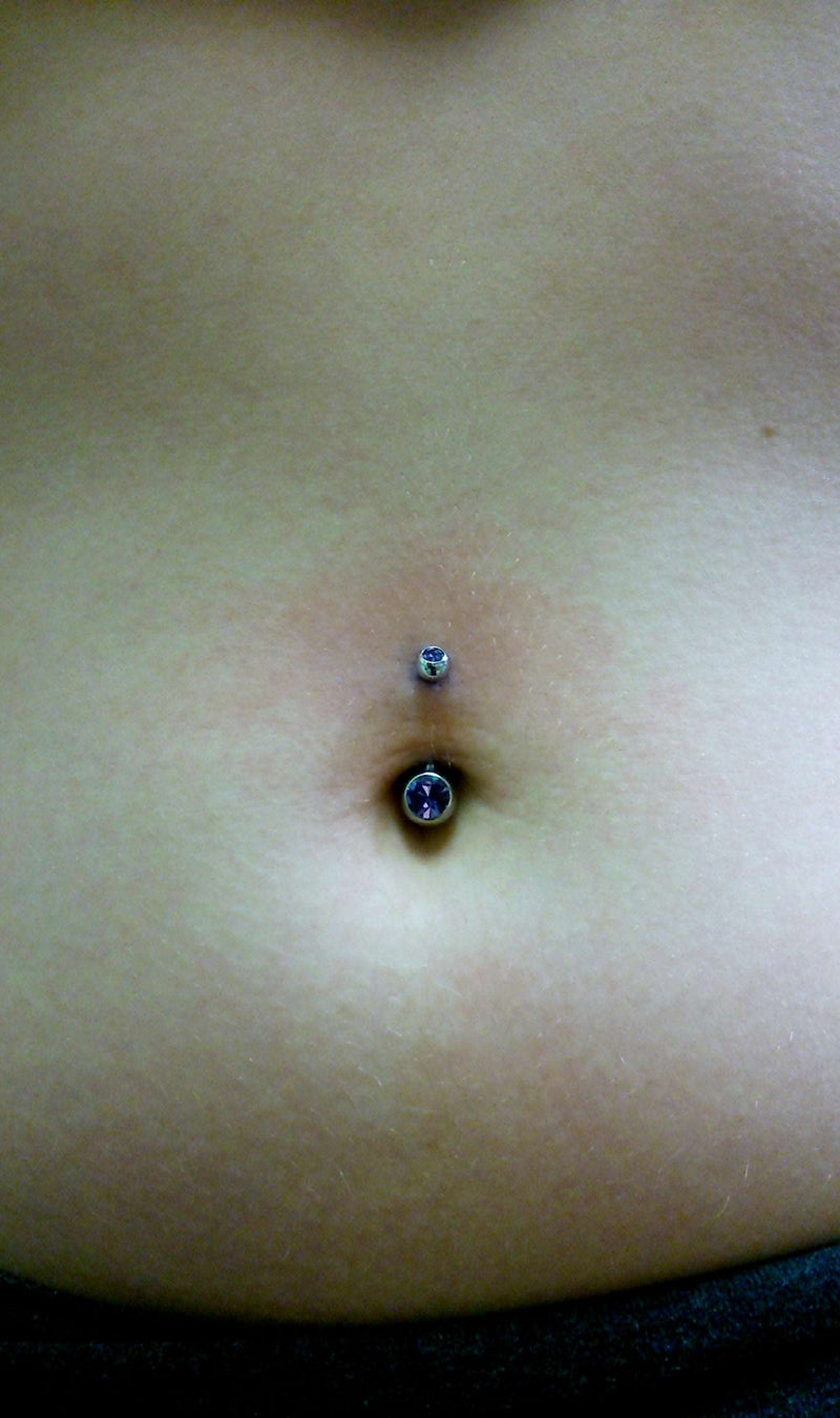Navel piercing done with our tribal made titanium curved barbells featuring a purple cz in a bezel setting on both the top and bottom beads
