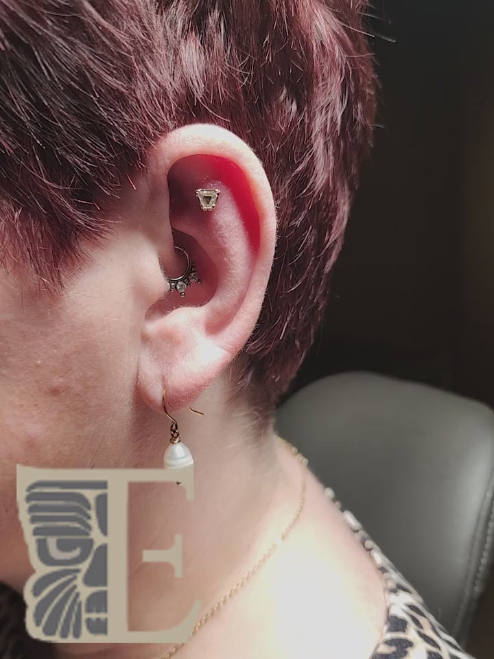 Angular upper-ear jewelry shown in a close-up piercing film